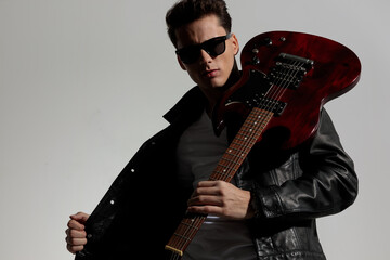 portrait of fashion man posing in a cool way with guitar over shoulder