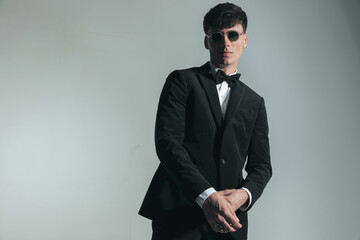 Obraz na płótnie Canvas elegant young guy in black tuxedo with glasses adjusting sleeve