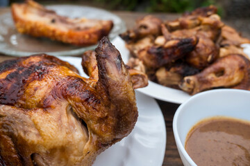 Plates of Lechon Manok or roasted chicken and Liempo or grilled pork belly, popular Filipino food served outside at a bench with gravy.