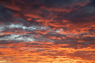 Fabulous sunset with clouds in intense radiant shades of crimson, purple and gold appearing ablaze and casting and ethereal glow over the entire sky, peaceful moment of the day before the nightfall