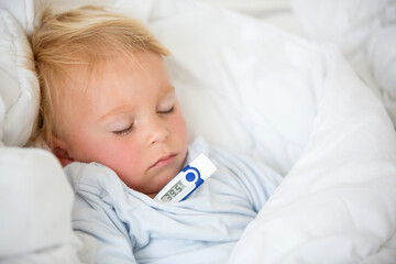 Tired toddler boy with high fever, lying in bed