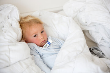 Tired toddler boy with high fever, lying in bed