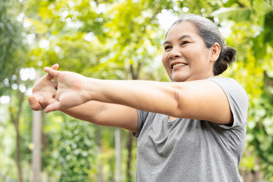 Old senior woman stretching arm and hand joint muscle, exercising in green park, breathing clean air, good and healthy life quality, self care and wellness concept image