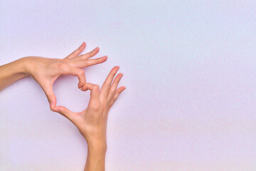 woman's hands making a heart gesture in the corner of the image with a bright white background