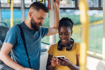Multiracial friends talking and using a smartphone while riding a bus in the city