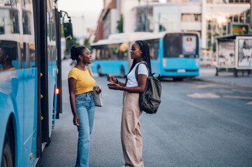 Couple of african american woman talking while waiting on a bus stop