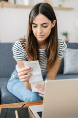 Vertical shot of young woman calculating household tax bills and expenses sitting on sofa at home
