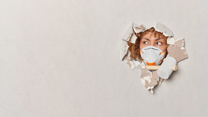 Female construction worker breaks through plaster wall wears protective respirator holds hammer focused aside busy doing house reconstruction. Blank copy space on white background for your promotion