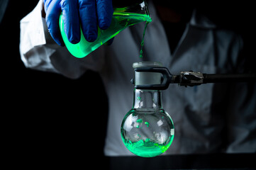 A woman scientist experimenting with a green fluorescent solution in a glass round bottom flask in dark chemistry laboratory