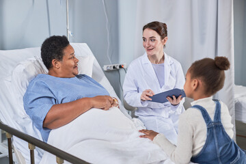 Fototapeta na wymiar Portrait of smiling young nurse talking to senior woman in hospital room