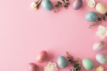 Beautiful Easter border from Easter eggs, flowers and green leaves on pastel pink background top view. Flat lay.