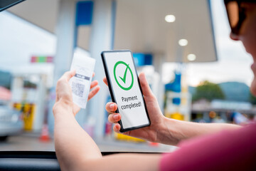 Woman using contactless payment by mobile phone with QR code at car filling station