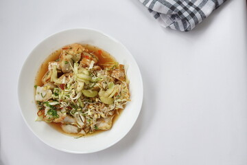 Kupat tahu is a traditional Indonesian food consisting of ketupat and tofu in peanut sauce. Usually include rice cake, tofu, bean sprouts, brown sugar, and prawn crackers. Served in white plate.