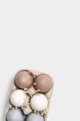 Close up Easter eggs pastel colored in egg box decorated small flowers. Minimal Easter celebration concept, dyed chicken egg with beige, white, grey colors in carton pack. Top view