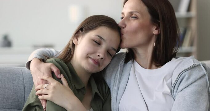 Close up loving mature woman enjoy tender moment, kiss, hugs her teenager daughter sit together on sofa. Happy motherhood, understanding and harmonic good friendly relations between teen child and mom