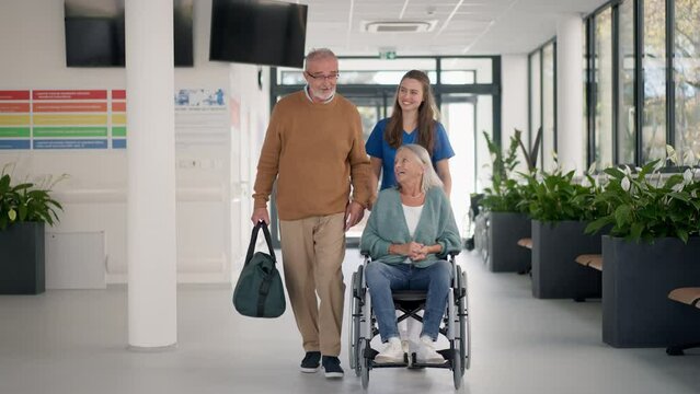 Young nurse talking with senior patients at hospital corridor.