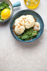Blue bowl with steamed cauliflower and spinach salad, vertical shot on a beige stone background, copy space, high angle view