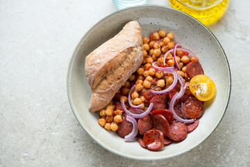 Stew with chorizo and chickpeas served with crusty bread on a beige stone background, horizontal shot, elevated view