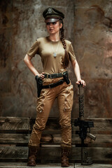 American pilot. A beautiful young woman in a uniform and with a weapon on the background of a metal wall. Staged photo. Studio light.