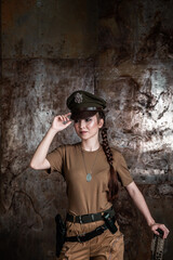 American pilot. A beautiful young woman in a uniform and with a weapon on the background of a metal wall. Staged photo. Studio light.