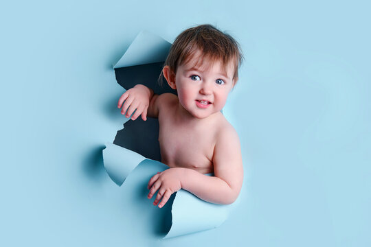 Happy Baby In A Hole On A Paper Blue Background. Torn Child Head Studio Background, Copy Space. Kid Aged One Year Six Months