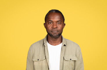 Fototapeta premium Calm serious confident mature black male in casual looking at camera, isolated on yellow background, studio
