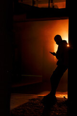 Silhouette of a masked man with a smartphone in orange smoke