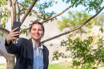 Businesswoman smiling while taking selfies with a mobile phone outdoors.