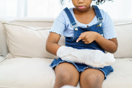 African American ethnicity girl showing and pointing to her injured or broken arm in bandage to camera. Black ethnicity girl have and accident at her arm.