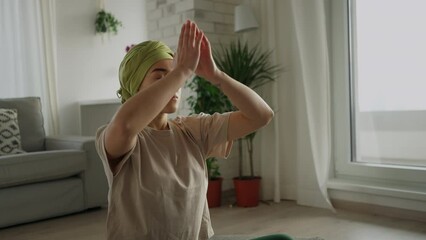 Young woman with cancer taking yoga and meditating in her apartment.