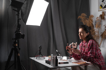 Happy young woman streaming a beauty vlog from home, online content creator teaching makeup on, recommending brushes