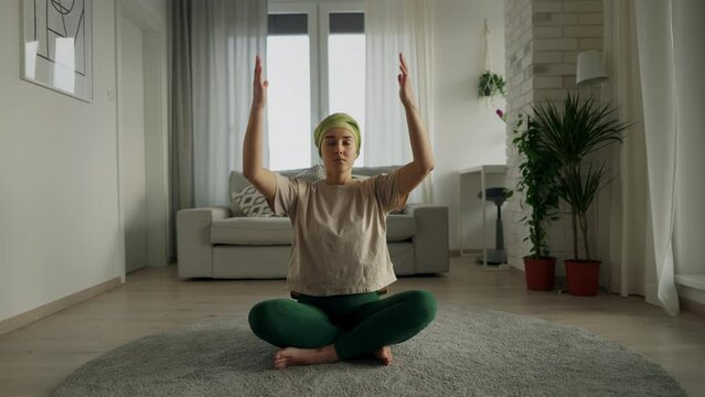 Young woman with cancer taking yoga and meditating in her apartment.