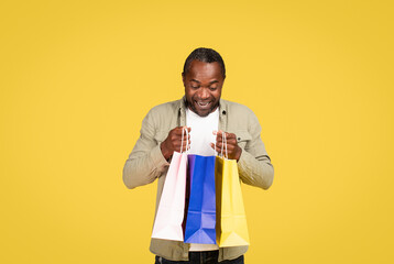 Glad shocked middle aged black male shopaholic in casual looking in package with purchases, enjoy fashion