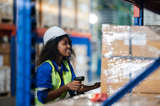 Woman employee of customs warehouse. Girl with box in warehouse. Customs storekeeper use laser scanner and tablet. female in safety helmet.