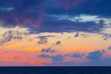 purple clouds in the setting sun with rich color palette and a dark blue sea
