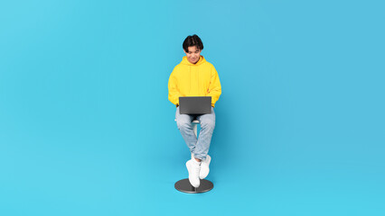 Korean Teen Guy Using Laptop Sitting Over Blue Studio Background