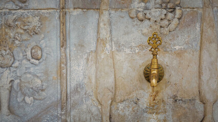 Brass faucet on a fountain with patterned marble wall, a public bronze faucet fountain in the old Ottoman traditional style. Vintage public fountain wallpaper