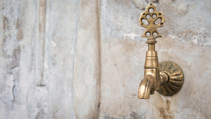 Brass faucet on a fountain with patterned marble wall, a public bronze faucet fountain in the old Ottoman traditional style. Vintage public fountain wallpaper