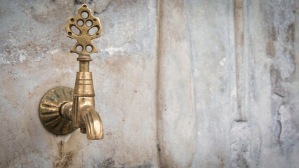 Brass faucet on a fountain with patterned marble wall, a public bronze faucet fountain in the old...