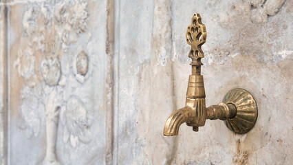Brass faucet on a fountain with patterned marble wall in the old Ottoman traditional style. Vintage public fountain wallpaper