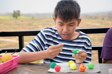 Fototapeta na wymiar Asian boy spending free time with modeling clays at home by sculpting plasticine into the shapes of animals, fruits and other things at home, soft and selective focus, copy space.
