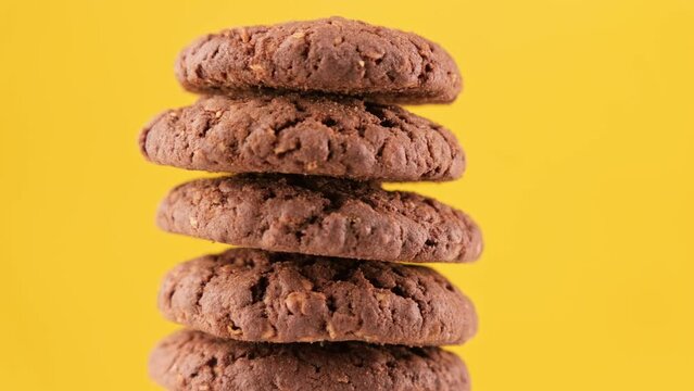 Rotating stack of fresh homemade cookies. Tasty bakery dessert. Pile of oatmeal cookies rotating on yellow background. Brown cookies. Food concept. Close-up in 4K, UHD