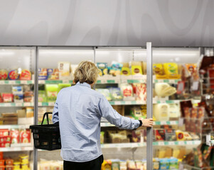  Man choosing frozen food from a supermarket freezer., reading product information