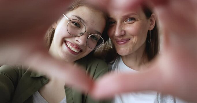 Close up happy faces of mature mother and teen daughter make heart sign with hands, enjoy close, tender moment together. Caring mom and grateful girl show love, express support in family relationships