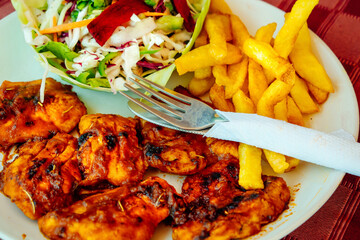 Grilled chicken, French fries and vegetable salad. A simple dish in a roadside cafe on a tablecloth background