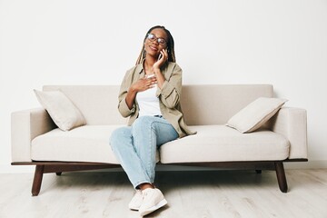 Fototapeta na wymiar African American woman business freelancer working sitting on the couch at home in the phone, business calls and messages happiness smile, home clothes and eyeglasses, light interior background.