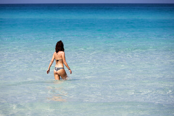 Fototapeta na wymiar Slim woman in bikini going to swim in blue sea water. Beach vacation on Caribbean islands