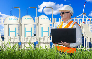 Hydrogen power plant technologist. Man with laptop near hydrogen plant. Getting electricity from wind and hydrogen. Man eco production technician. H2 storage tanks behind engineer.