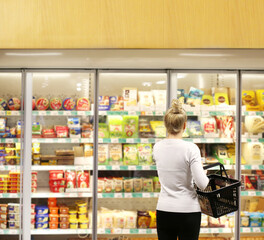 Woman choosing frozen food from a supermarket freezer, reading product information