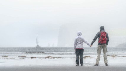 Ein Pärchen steht am Strand von Tjørnuvík mit Blick auf die Felsnadeln von Risin und Kellingin...